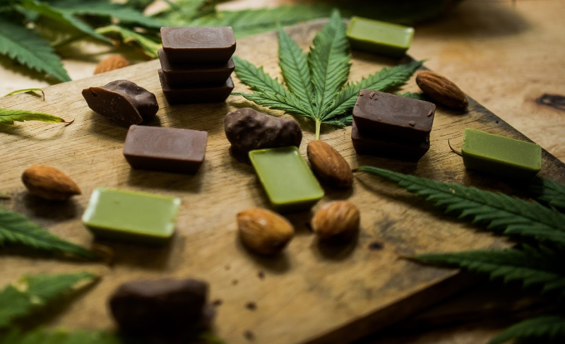 Assorted cannabis-infused chocolates and confections arranged on a wooden board with cannabis leaves and almonds.