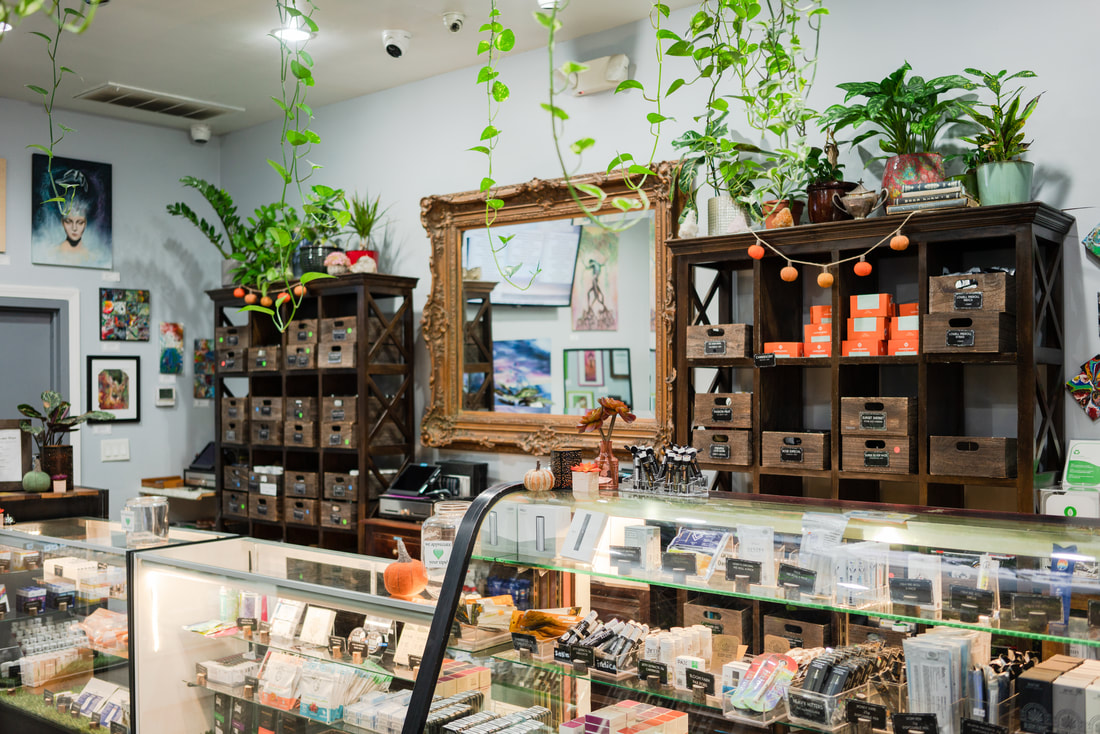 Interior of a modern cannabis dispensary with glass display cases, wooden shelves, hanging plants, and packaged products on display.