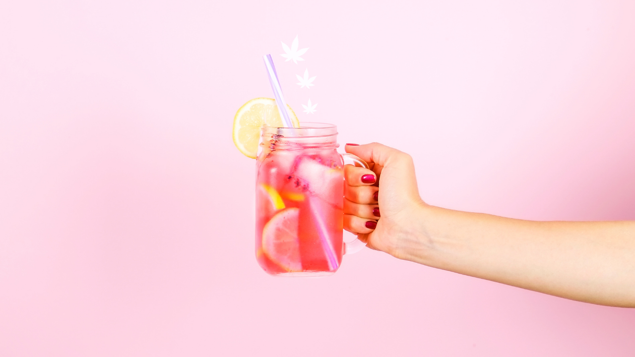 Hand holding a mason jar of pink lemonade with lemon slices and a straw against a pastel pink background, with small cannabis leaf icons floating above the drink.