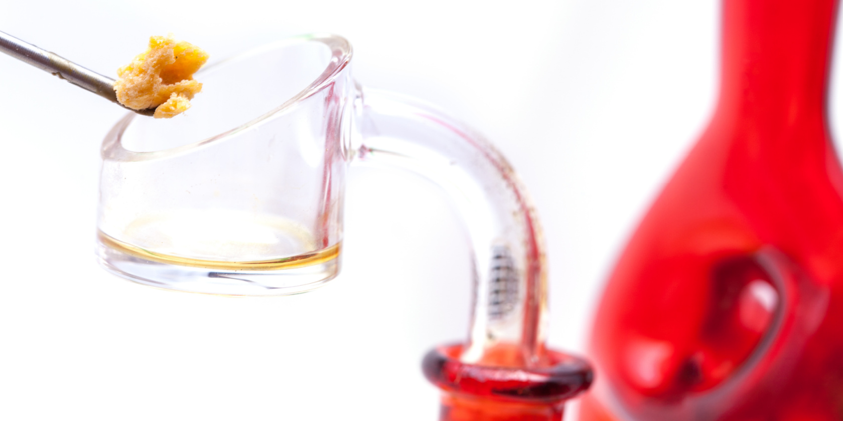 Close-up of a glass dab rig with a metal tool holding cannabis concentrate above a clear quartz banger.