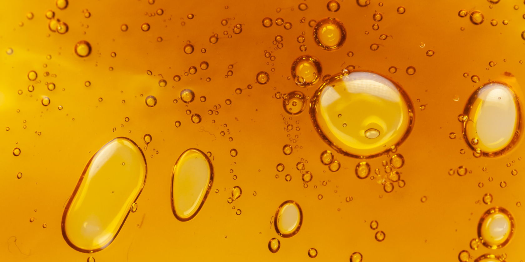 Close-up of golden oil droplets suspended in liquid, creating an abstract textured background.