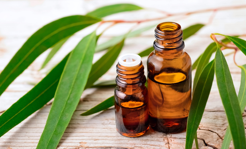 Two small amber glass bottles with open caps placed on a wooden surface, surrounded by green leaves.