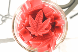 Top-down view of red cannabis leaf–shaped gummies inside a clear glass jar.