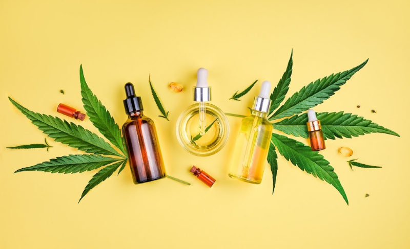 Cannabis oil dropper bottles arranged with green cannabis leaves on a yellow background, representing CBD or hemp extract products.