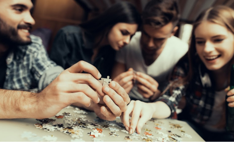 Group of friends sitting together and working collaboratively on a jigsaw puzzle at a table.