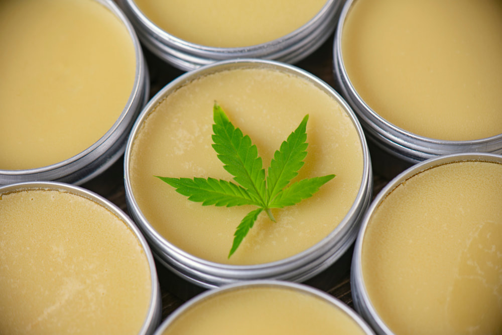 Open tins of cannabis-infused balm with a green cannabis leaf placed on the center container.