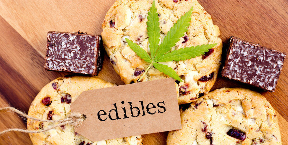 Cannabis-infused cookies and chocolate edibles arranged on a wooden board, topped with a green cannabis leaf and a tag labeled edibles.