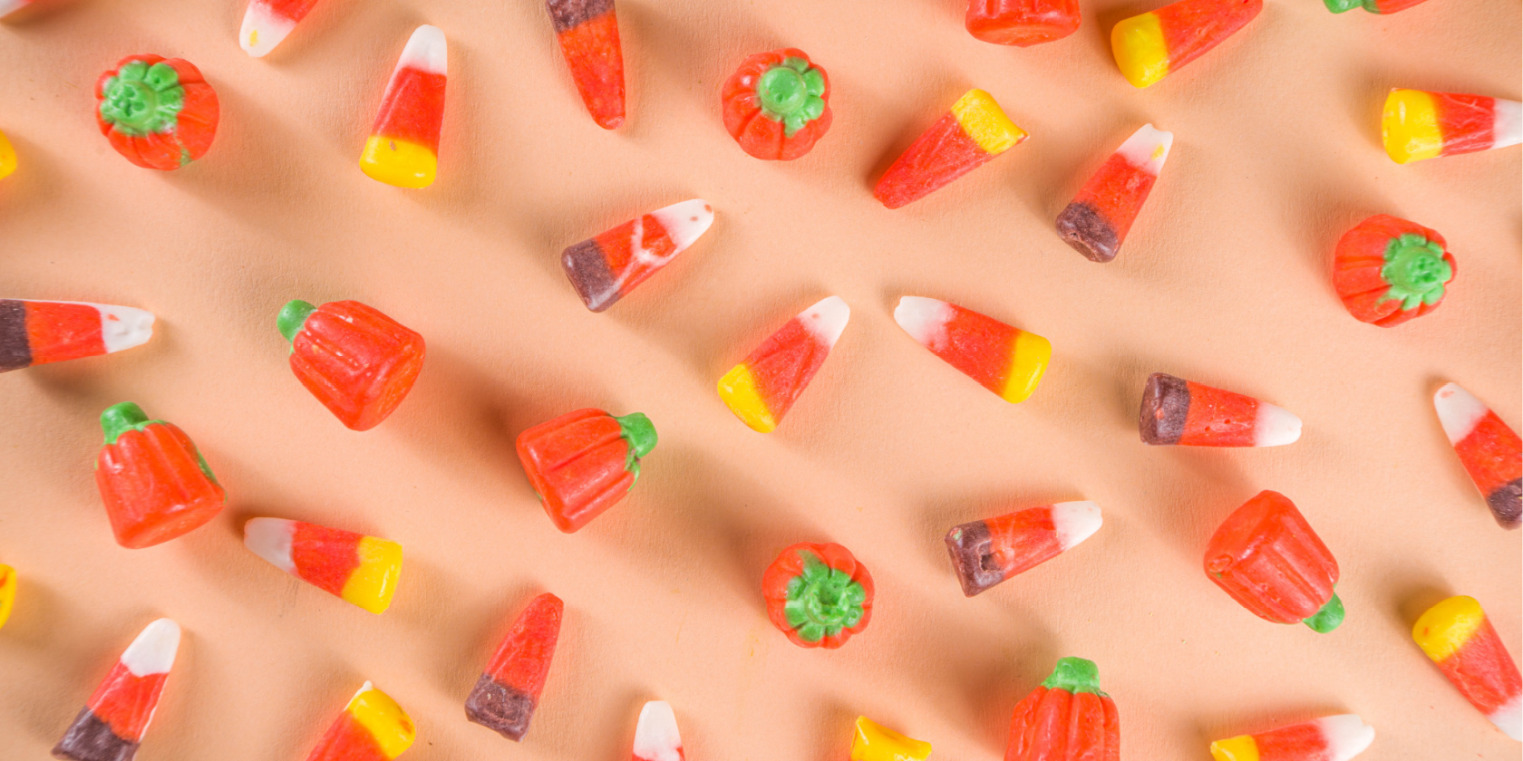 Pattern of candy corn and small pumpkin-shaped candies scattered on a peach-colored background.
