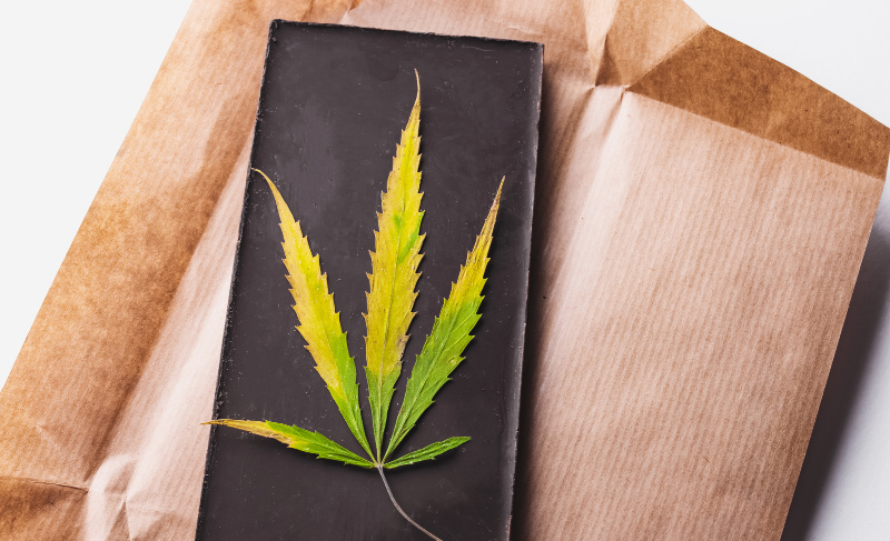 Cannabis leaf placed on a dark rectangular surface surrounded by brown paper packaging.