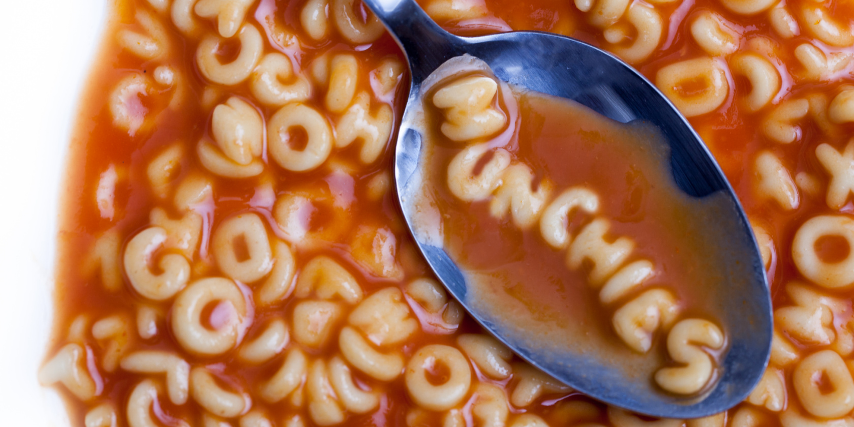 An image of a metal spoon lifting alphabet soup that spells out the word MUNCHIES in tomato sauce.