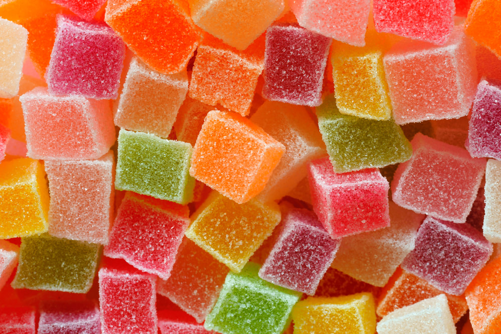 A close-up, top-down view of numerous sugar-coated gummy cubes in a variety of bright colors like pink, orange, yellow, and green.