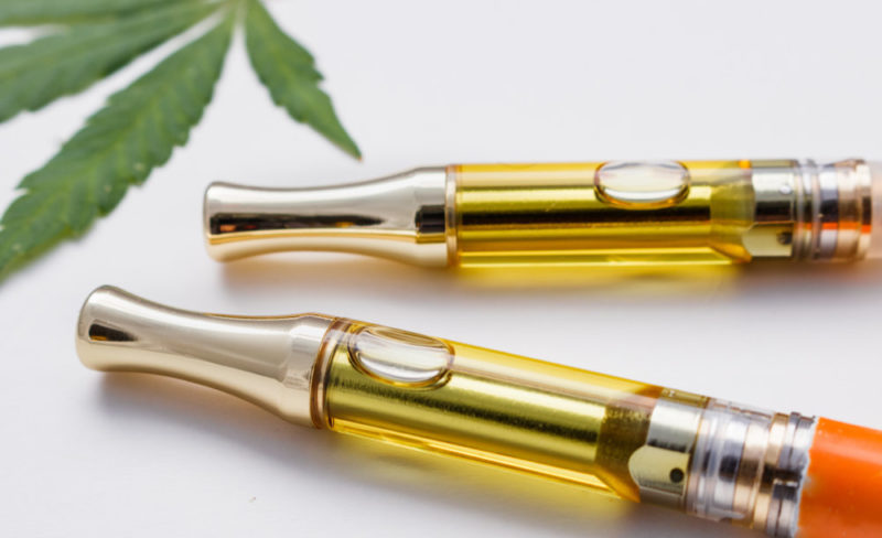 Two cannabis oil vape cartridges filled with golden liquid, with a cannabis leaf partially visible in the background.