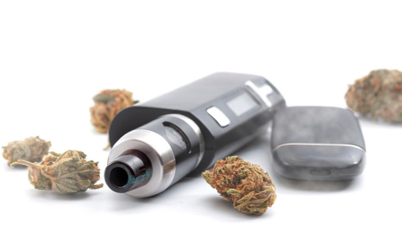 Vape device placed on a white surface alongside several cannabis buds.